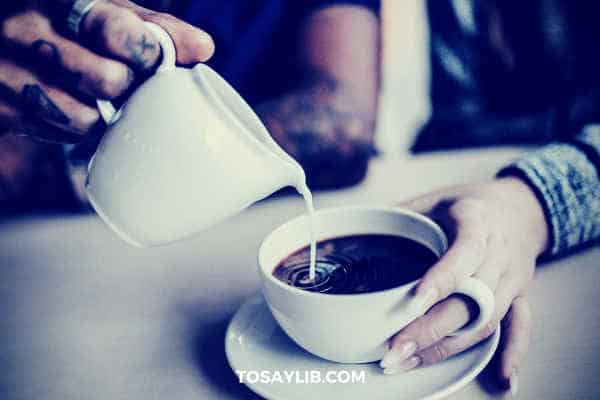 man pouring milk into coffee for lady