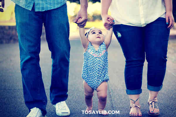 parents holding hands of a baby girl on each side walking