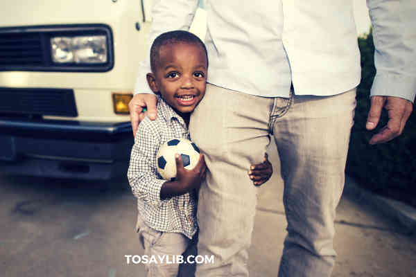 little boy holding a football and leg of his dad