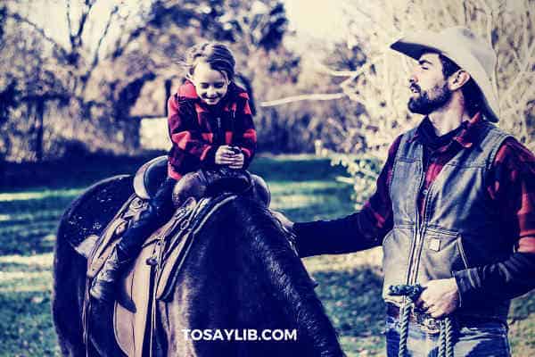 dad teaching daughter how to ride on pony