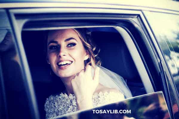 bride sitting in the car smiling watching invitees