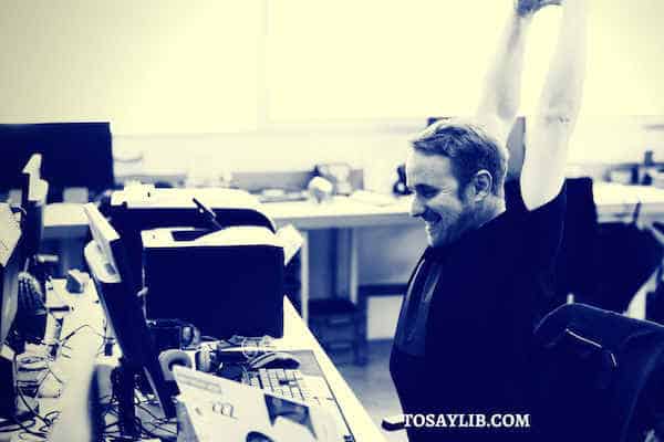 man stretch hands over head smiling laptop office