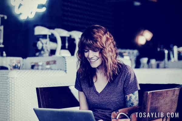 женщина в кафе смотрит на ноутбук улыбается