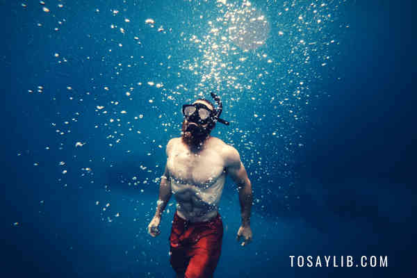 man diving in water holding breathe