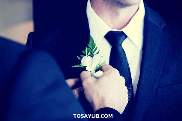 best man helping groom putting flower bouquet on suit