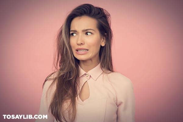 13 Woman standing against a pink wall looking uncertain