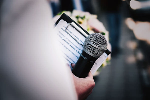 08-Featured-Photo-of-a-person-holding-a-microphone-while-holding-a-clipboard-and-a-boquet-of-flowers