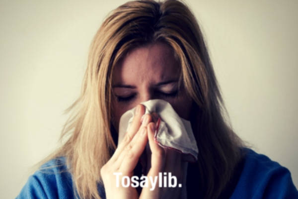 Woman in blue sweater blowing nose handkerchief gray background