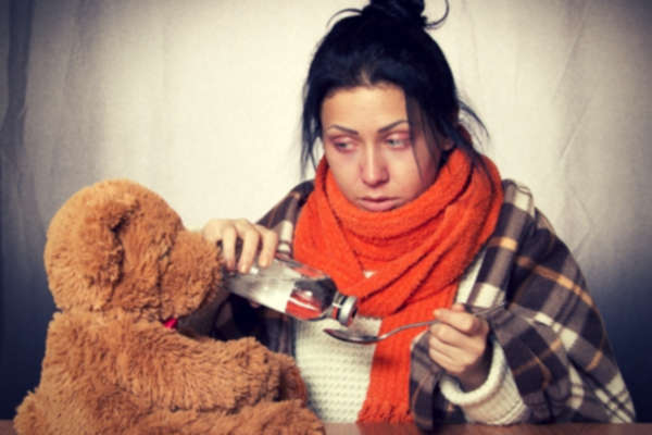 12-feature-woman-in-sweater-blanket-sick-taking-medicine-teddy-bear-table-gray-background