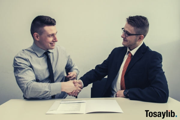 two man business attire hand shake documents table