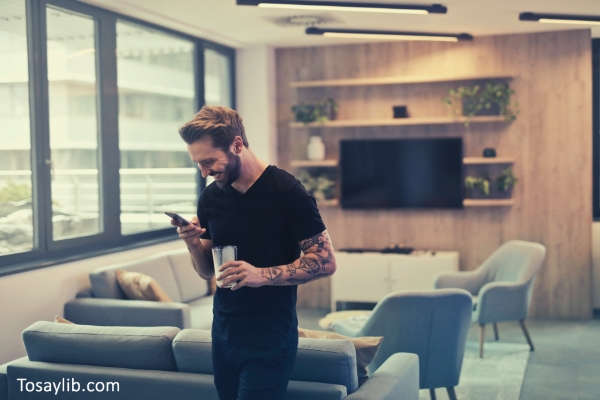 man-in-black-shirt-standing-while-holding-drinking-glass-texting-smiling