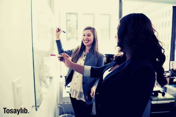 two women in front of dry erase board writing smiling office