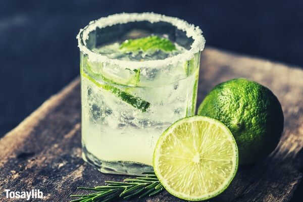 sliced lime fruit near clear drinking glass with lime juice on brown wooden plank