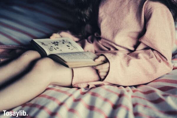 girl wearing pink dress sitting on bed reading book