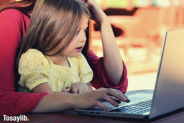 brunette woman in red with girl in yellow on lap before laptop