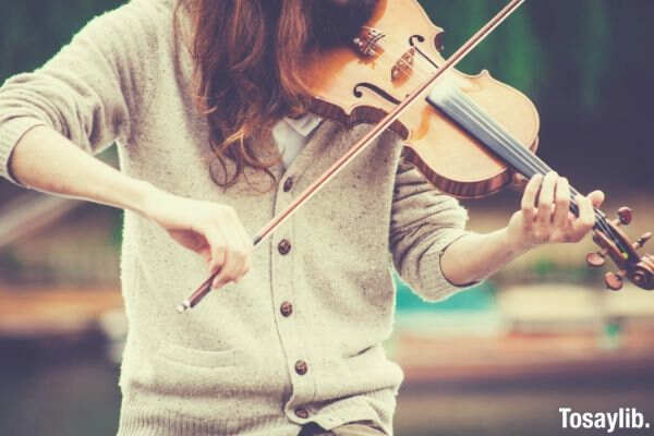 woman in gray cardigan playing a violin during daytime