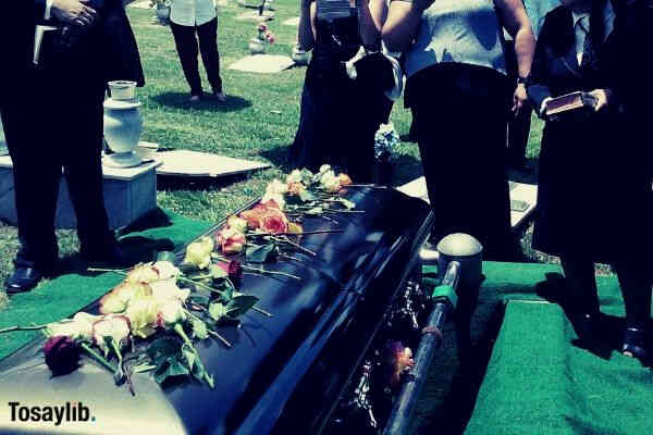 flowers on top of coffin mourning people wearing black