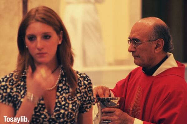 woman wearing red sad priest giving communion