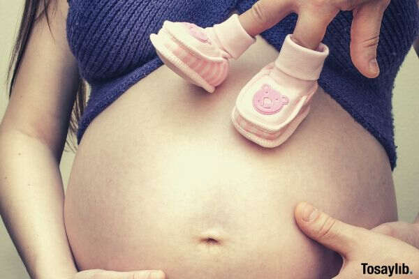 pregnant woman belly baby shoes on fingers