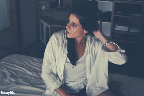 woman in white sitting on the bed scratching head