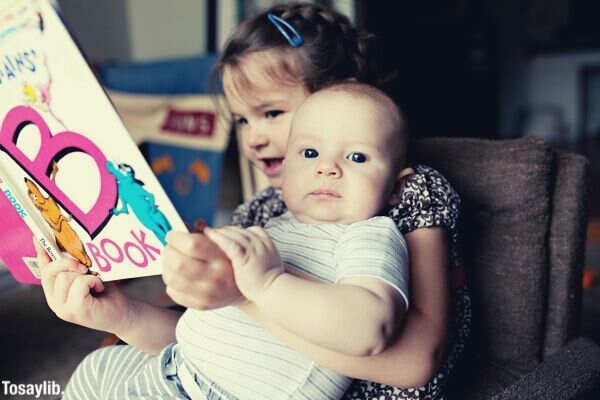 little girl reading book to baby brother