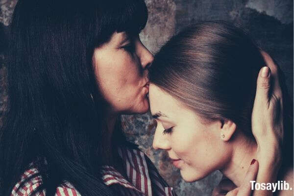 mother kissing daughter s forehead