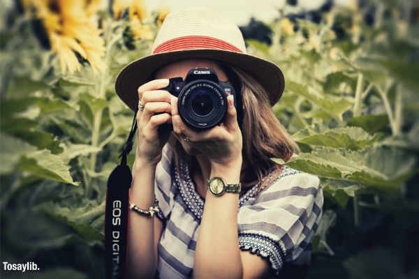 selective focus photography of woman holding dslr camera sunflower plant