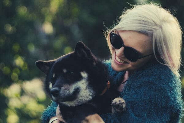 woman-sunglass-bluegreen-coat-holding-black-dog