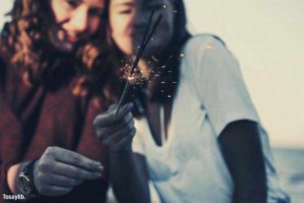 sunlight sunset teenager best friend golden hour sisterhood girl laughing holding stick of lights