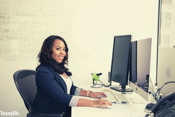 woman wearing black cardigan sitting on black mesh back rolling armchair and using silver imac