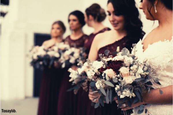 shallow focus of women holding white flower bride bridesmaid red gown