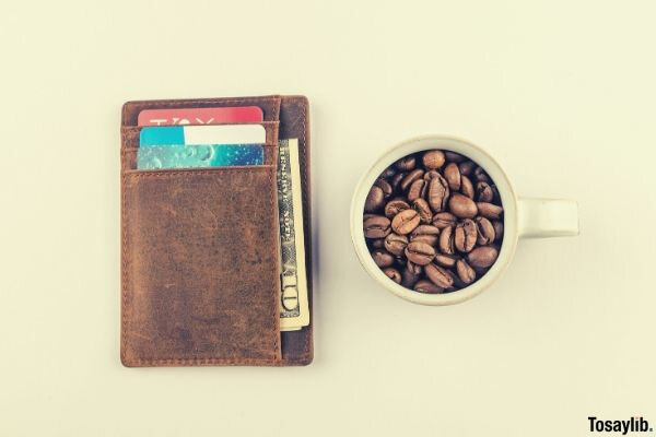 white mug with coffee beans beside brown wallet