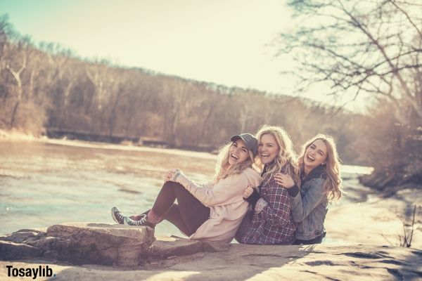 three woman sitting on rock smiling river trees