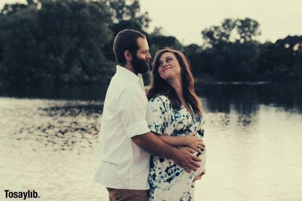 husband hugging pregnant wife smiling river trees