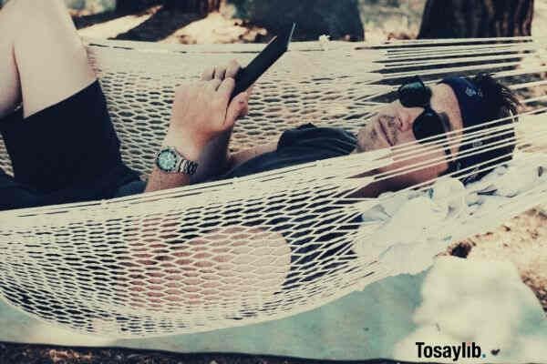 man wearing black shirt lying on white hammock