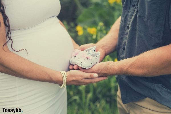 couple holding white baby shoes flowers grass