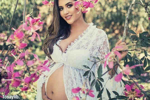photo of pregnant woman near purple flowers trees baby bump white dress
