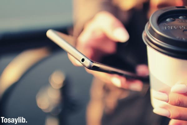 woman using smartphone holding coffee