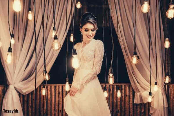 woman standing beside hanging light bulbs white gown curtain wood