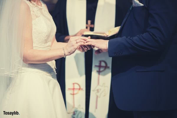 man woman wedding holding hand wearing ring priest