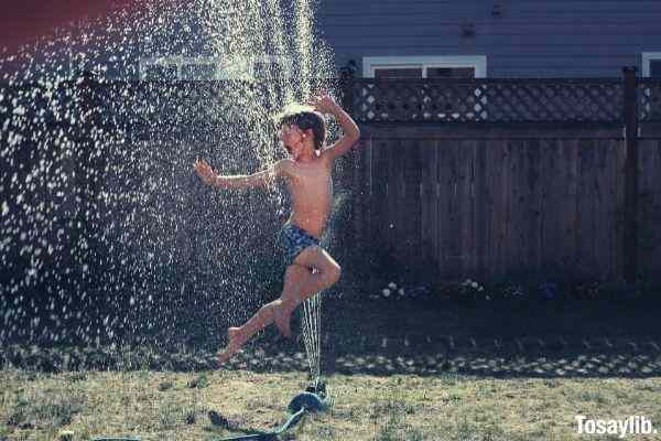 boy jumping on water sprinkler