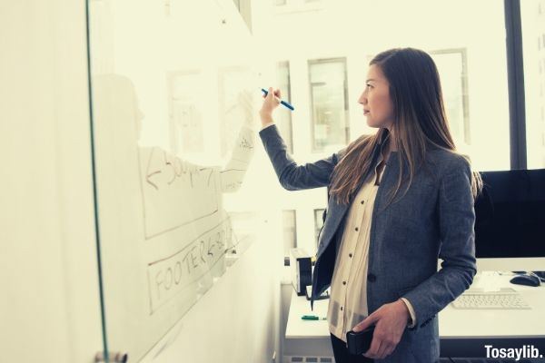 woman wearing gray blazer writing on dry erase board