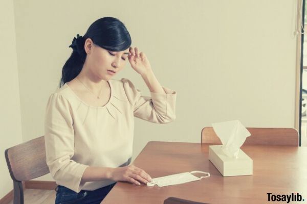 sick woman holding her head tissue facemask