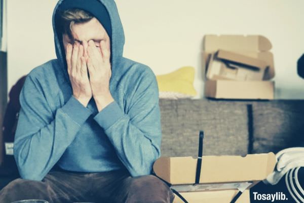 man covering face with both hands while sitting on the sofa