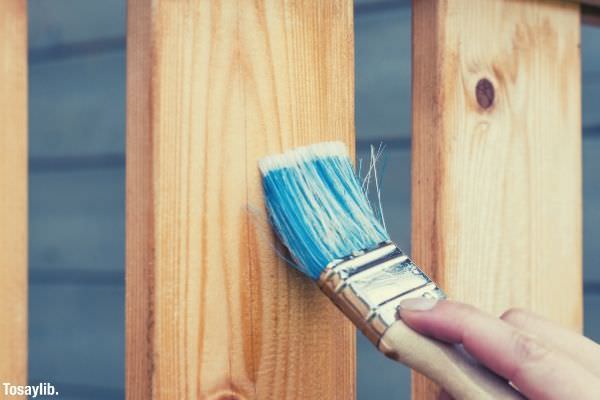 person holding paint brush painting wood