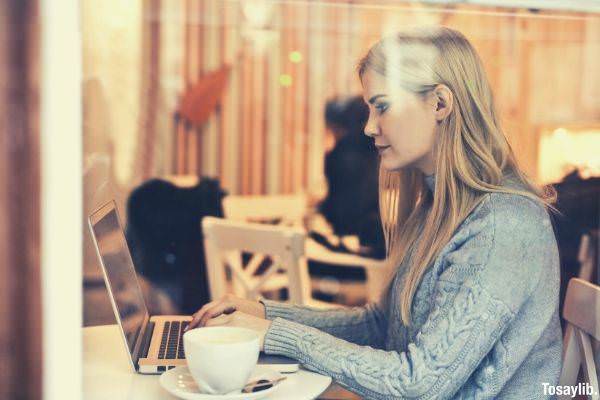 serious young woman using netbook while having hot drink in modern cafe