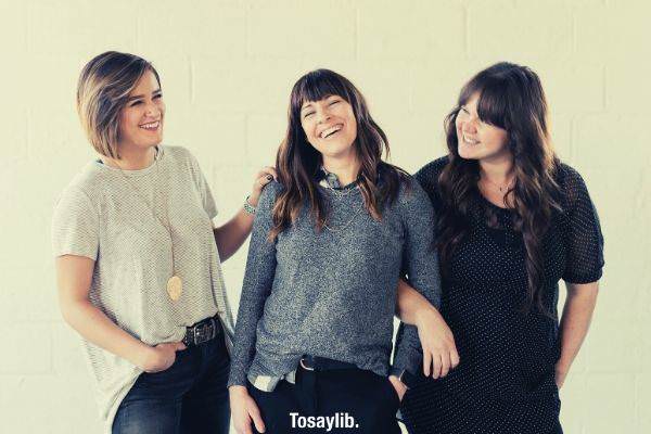 three women smiling and standing near white wall