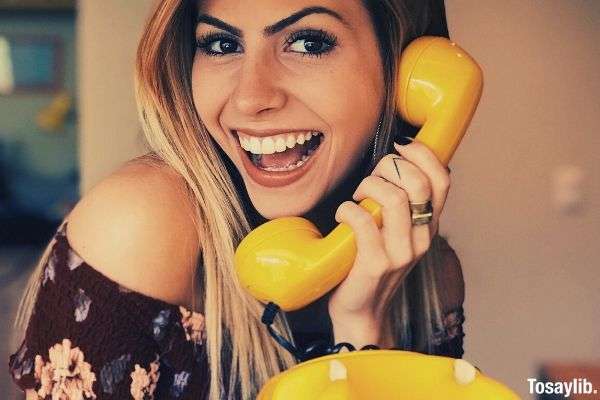 woman wearing off shoulder holding yellow rotary telephone