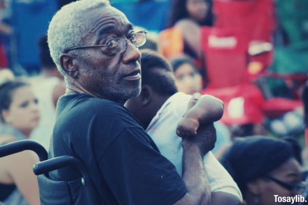 grandpa sitting on wheelchair holding a baby crowd