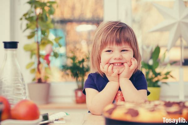 photo of a toddler smiling on the camera in front of food wearing purple shirt